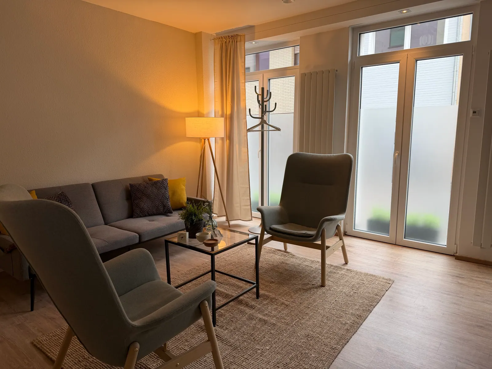 Praxisraum Brühl im Tageslicht: zwei Sessel, niedriger Tisch, Sofa, große Fenster