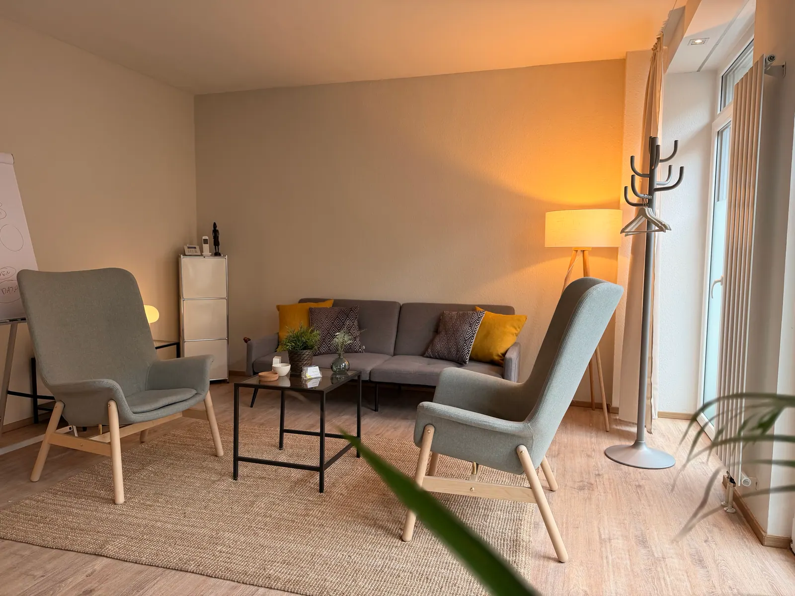 Praxisraum in Brühl: zwei Sessel und ein Sofa um einen niedrigen Tisch, abendliches Licht durch große Fenster